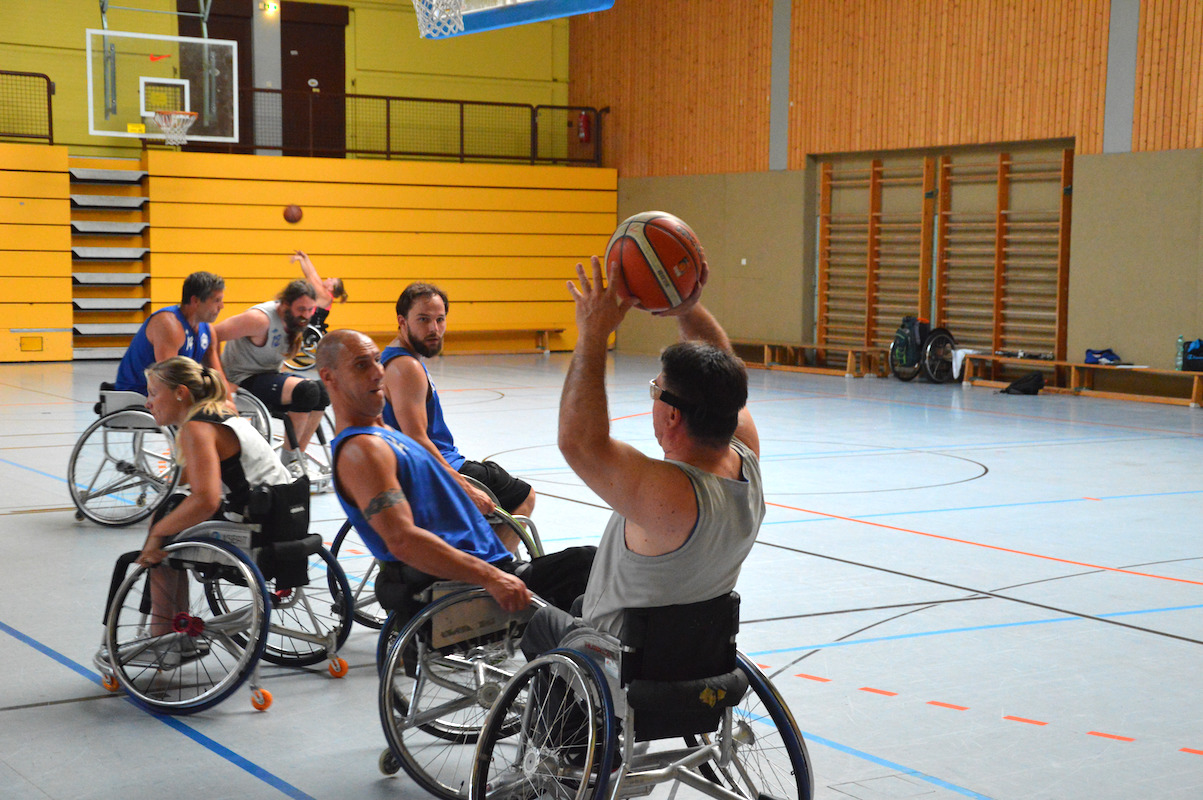 sechs Rollstuhlbasketballer spielen intensiv auf einen Korb Streetball